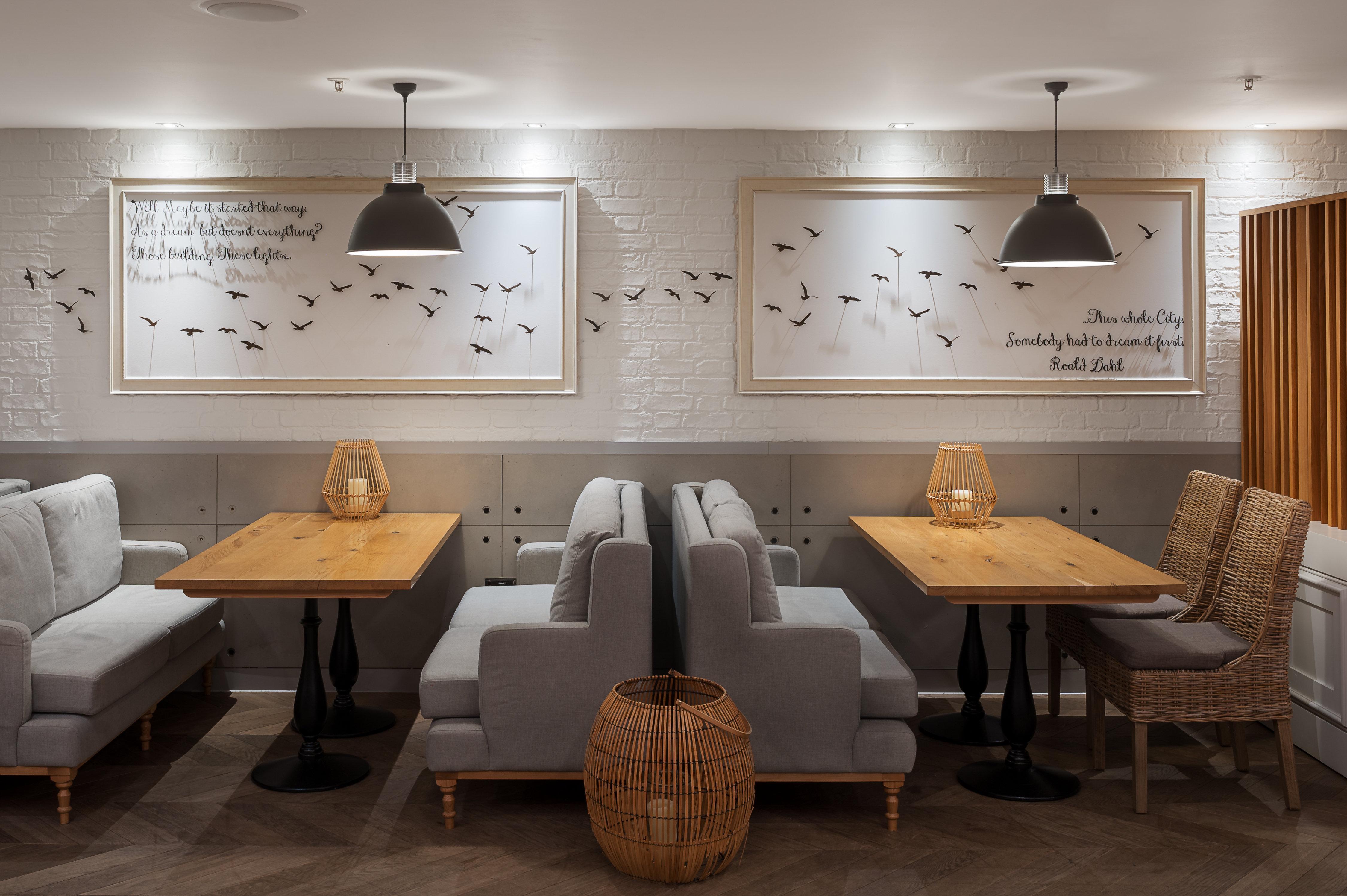 فندق فوكو سانت دايفيدز كارديف المظهر الخارجي الصورة The photo shows a modern and stylish interior of a café or restaurant. There are wooden tables paired with comfortable seating, including gray benches and wicker chairs. The walls are adorned with two framed artworks featuring bird silhouettes, accom